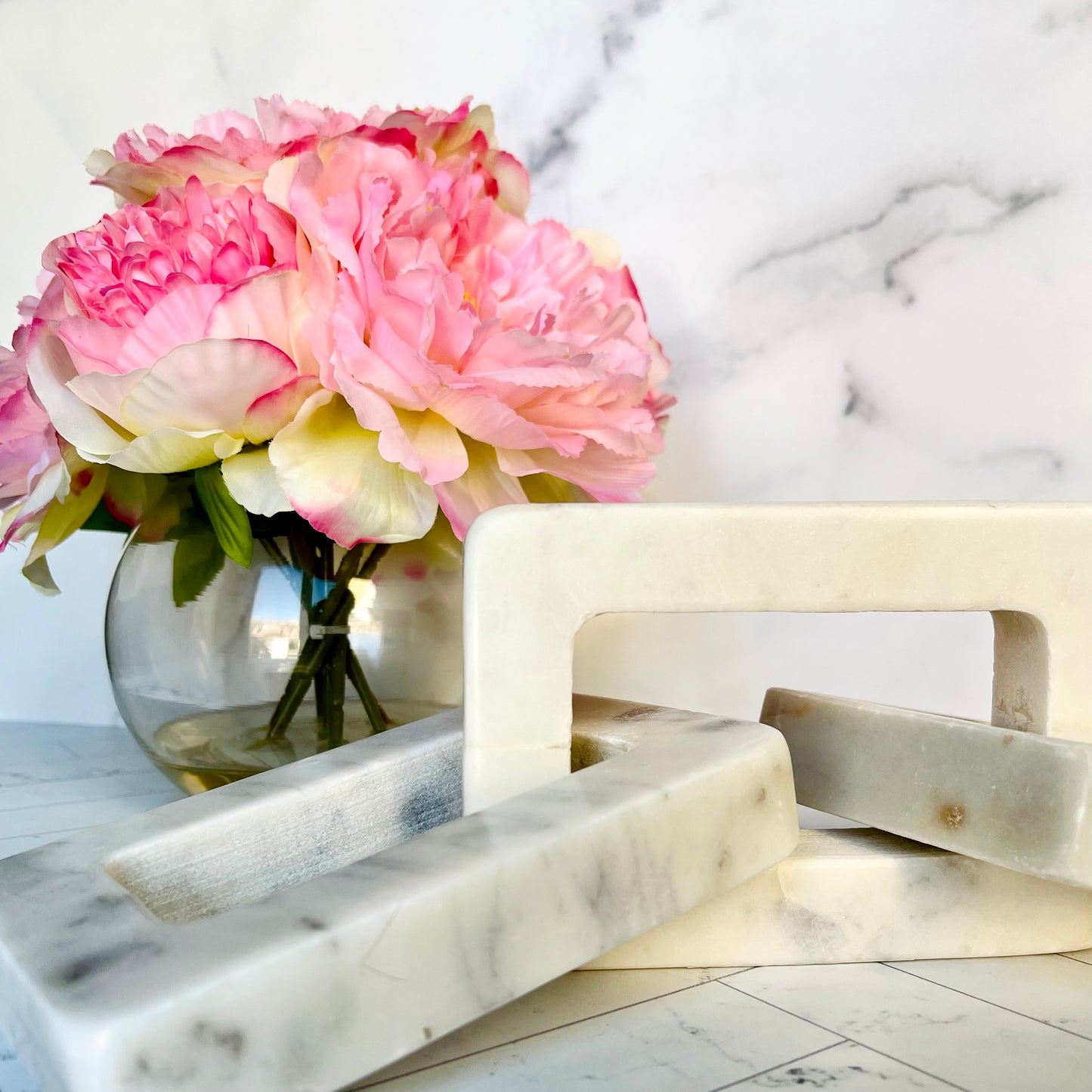 A white marble decor chain with a vase of pink peonies behind it