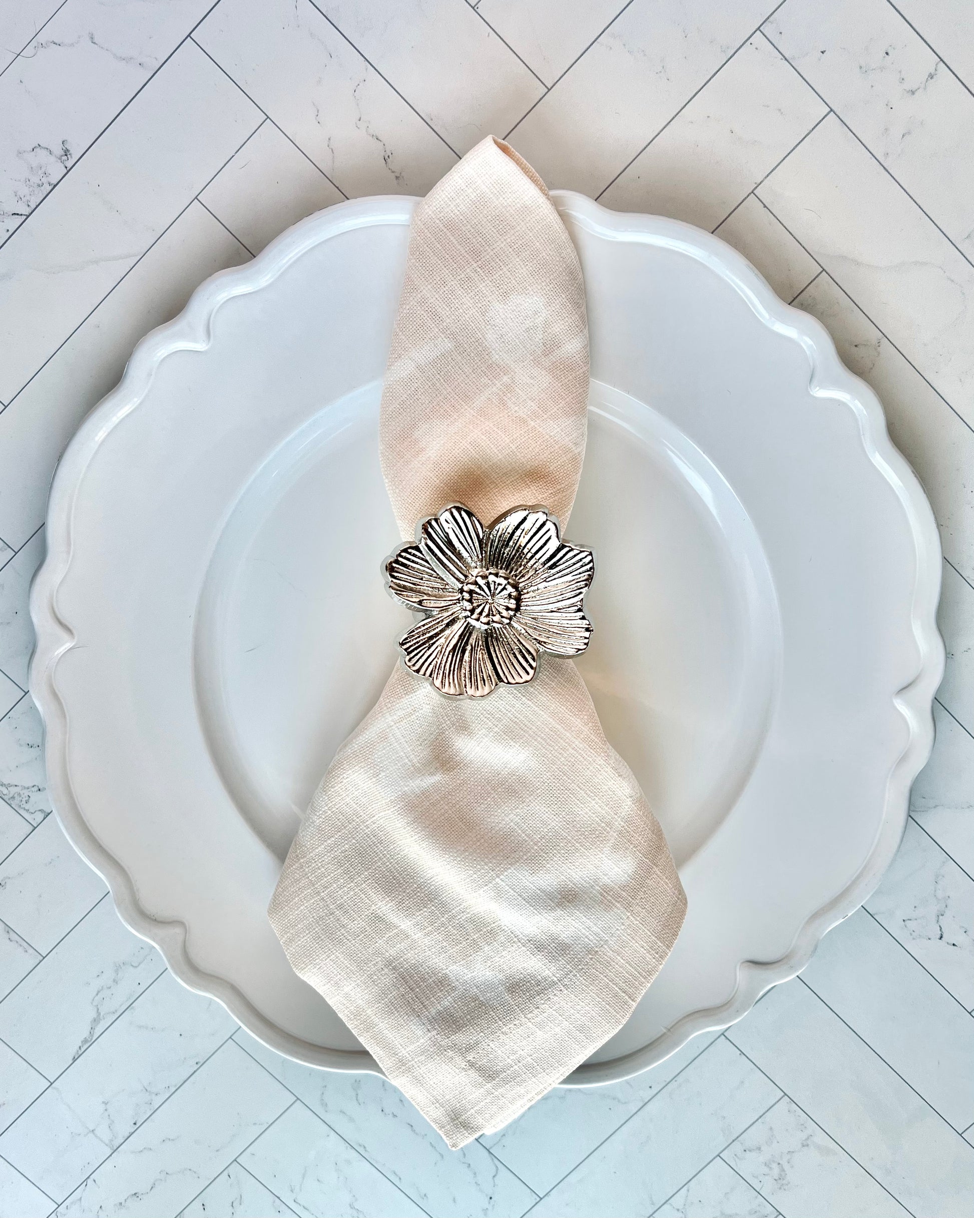 A pink floral napkin wrapped inside a silver flower napkin ring on a white plate