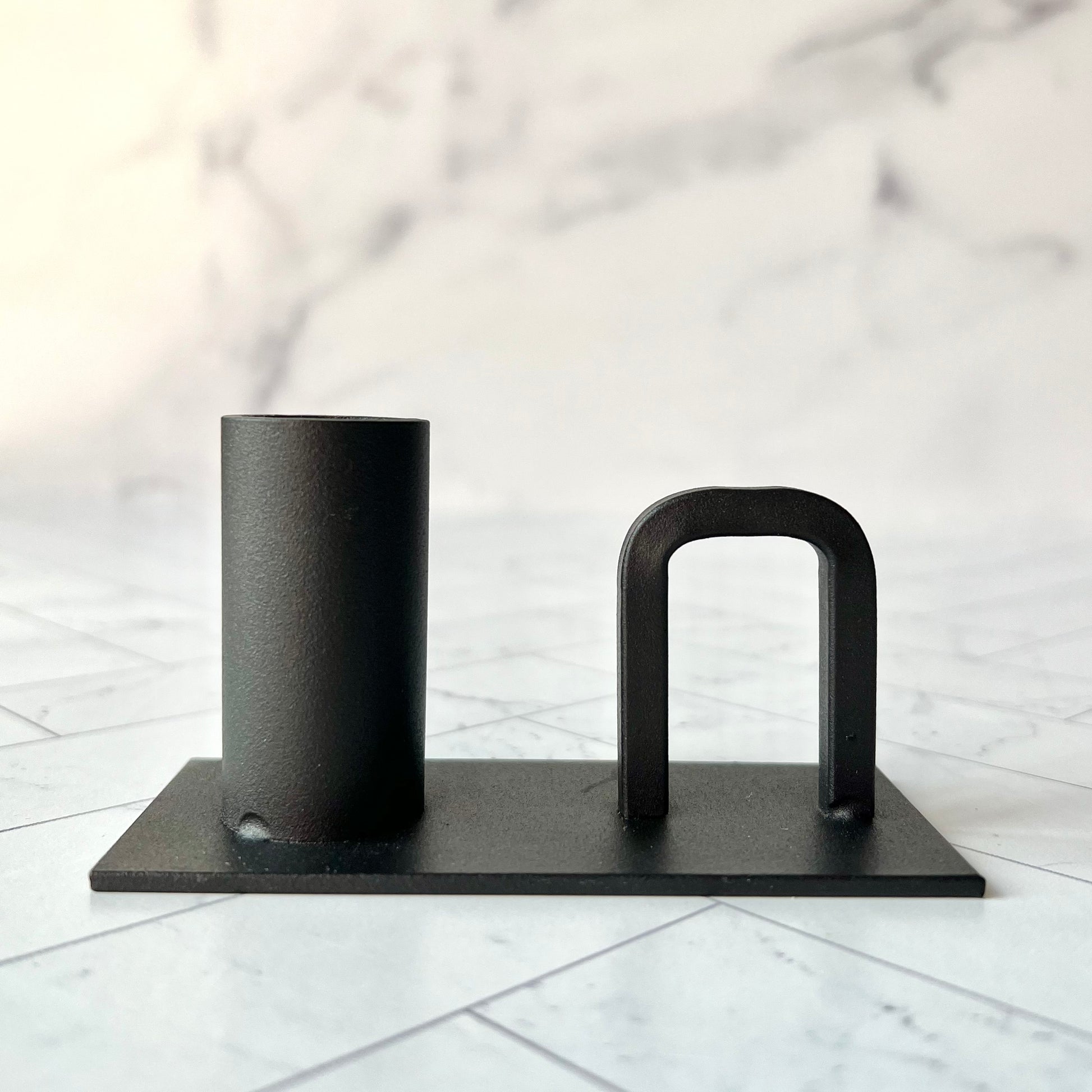 A black candlestick with a handle on it on a white surface - The Offbeat Co.