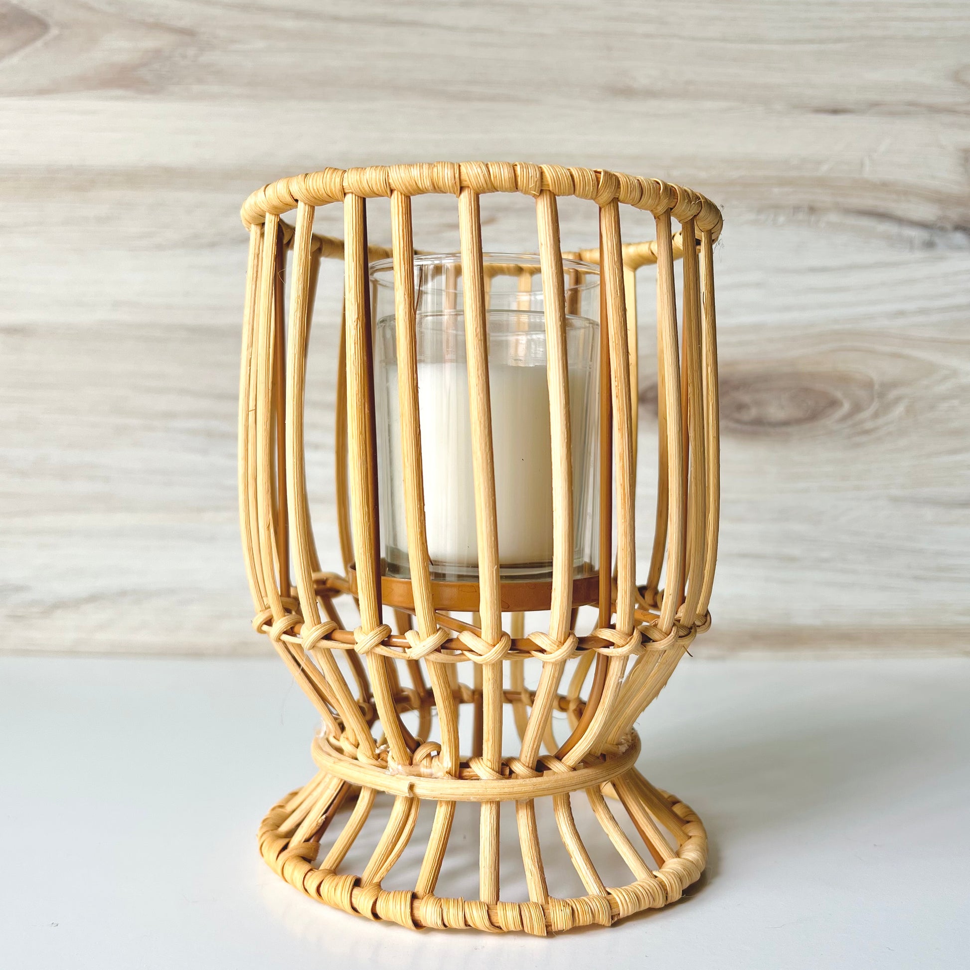 The Rattan Candle Holder on a white surface with a wooden wall behind - The Offbeat Co.