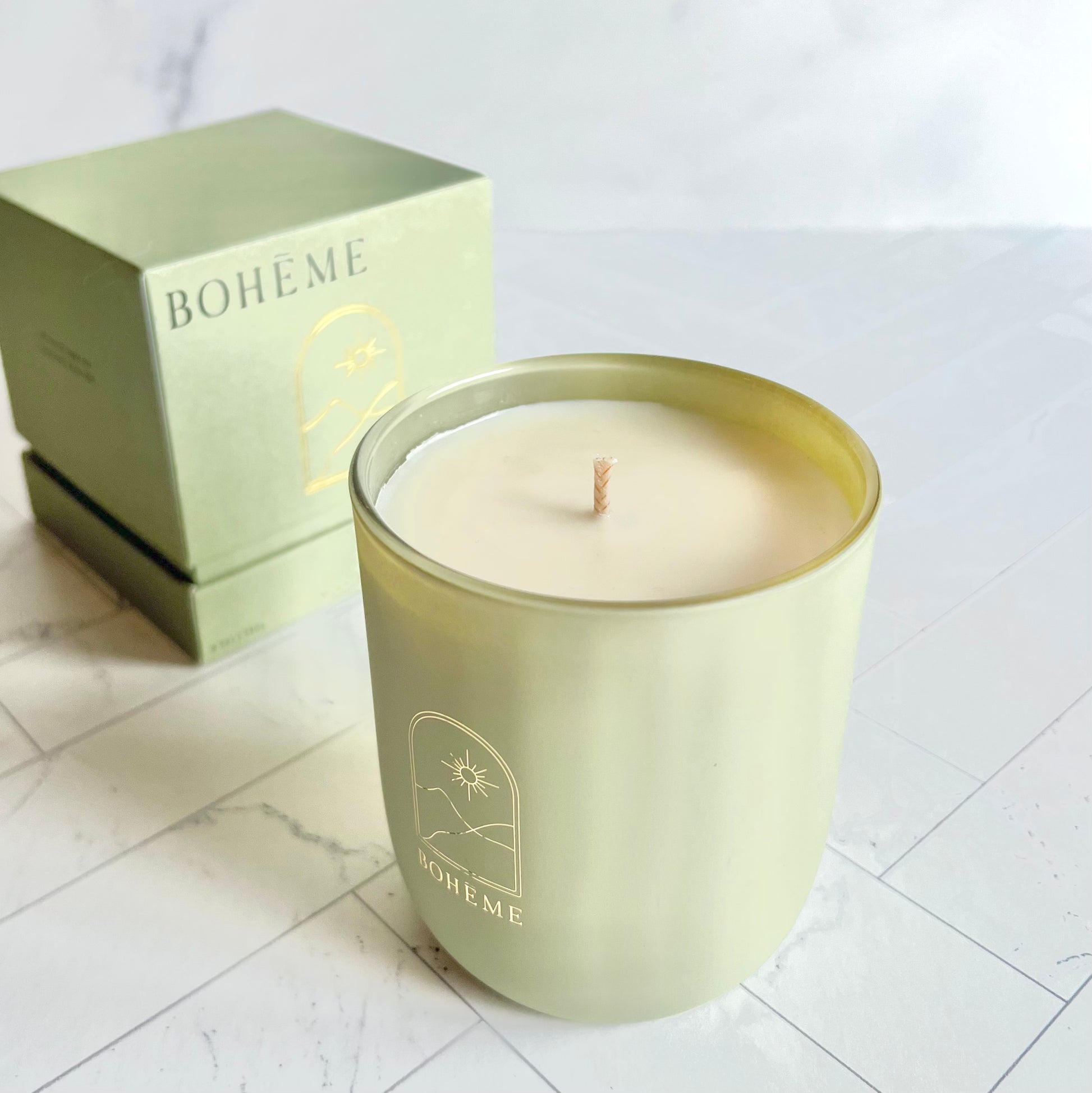 A light green candle with its box behind on a white surface