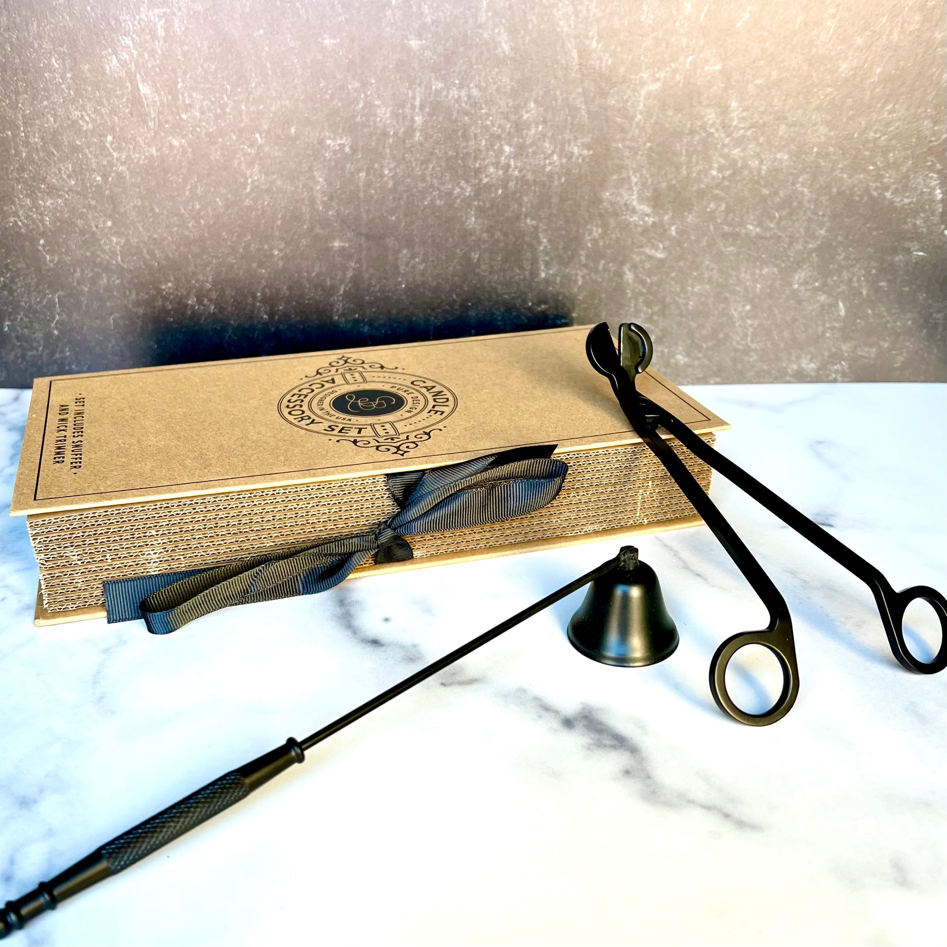 The Candle Snuffer & Wick Trimmer sitting on a table with the box they come in behind