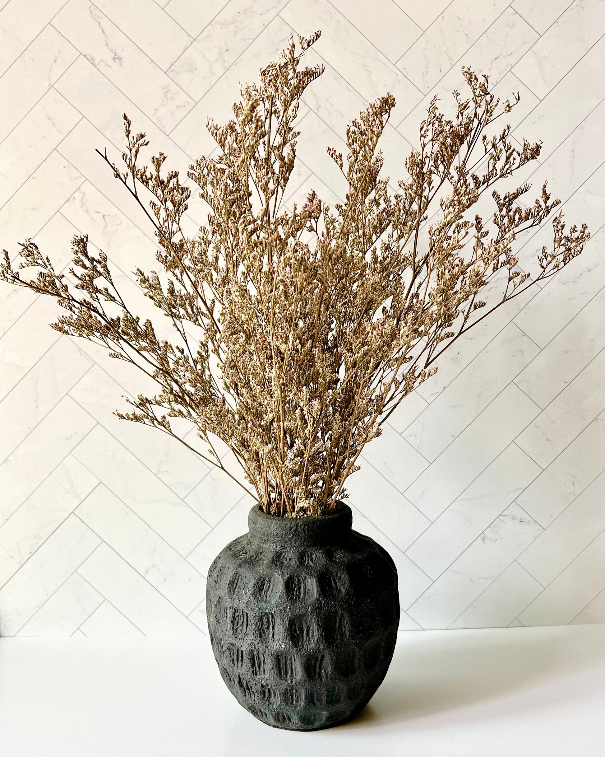 The Limonium Dried Flowers in a small black vase against a light background