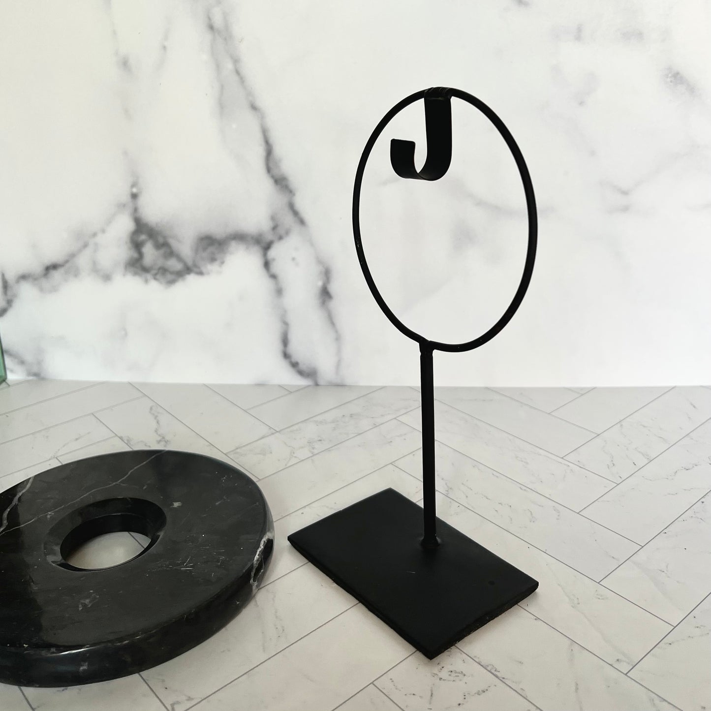 The marble black disc laying on a light surface with its stand next to it to show the stand's structure