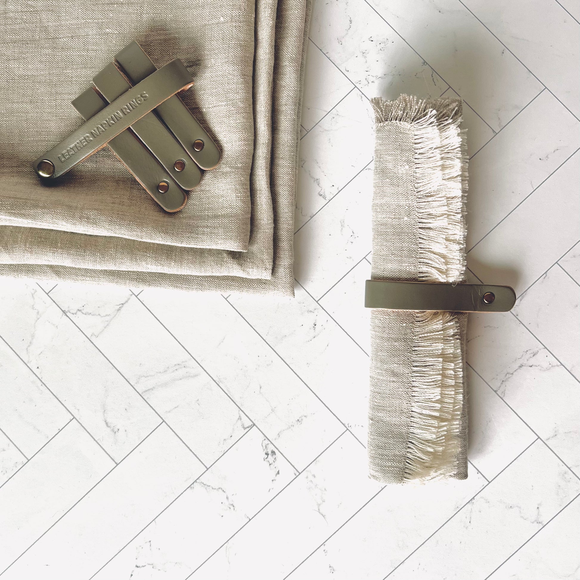 A Gray Leather Napkin Ring around a beige napkin with the other napkin rings on the side - The Offbeat Co.